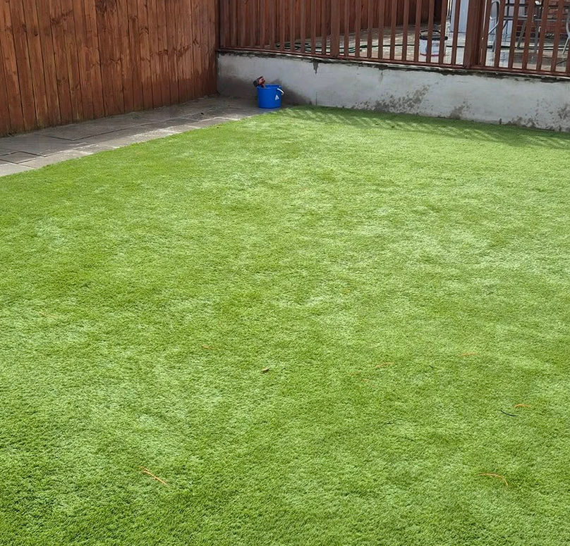 A lush, green artificial lawn fills most of the image, bordered by wooden fencing
