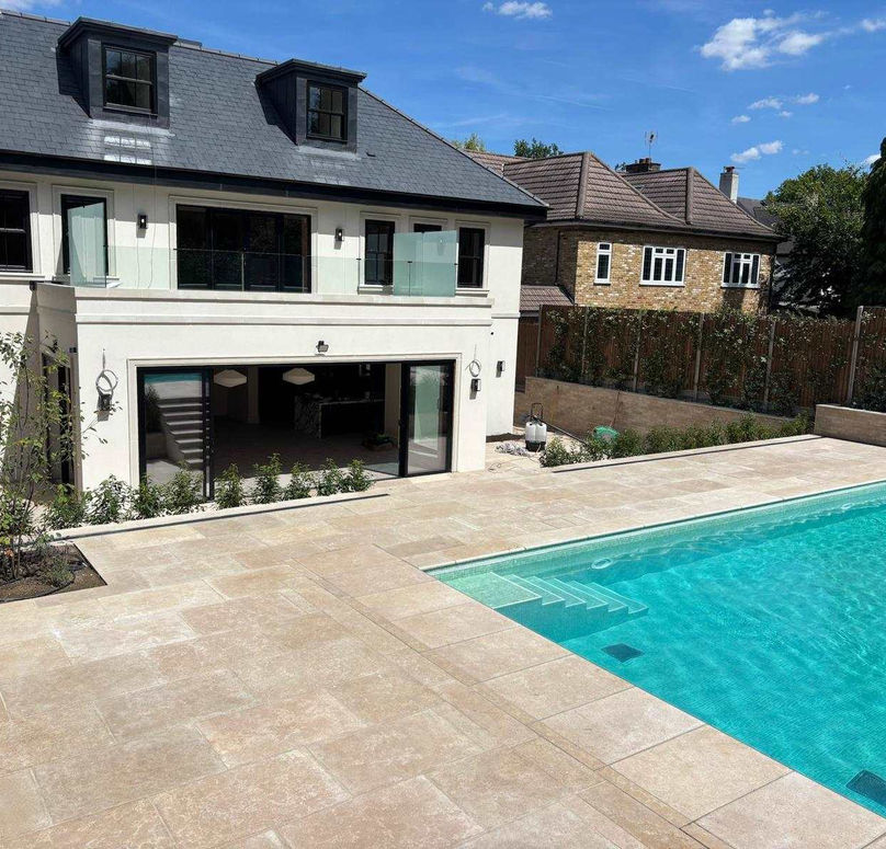 Modern white house featuring a beige stone patio and a luxury turquoise swimming pool under a blue sky