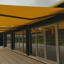 A modern building with large glass doors is shaded by a bright yellow awning