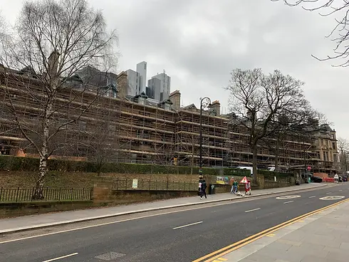 Scaffolding on a long brick estate building next to a street with trees in Scotland