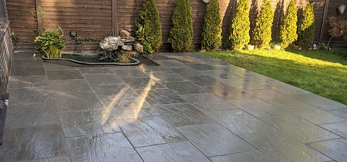 A patio featuring a stone floor and a tranquil water feature, surrounded by greenery