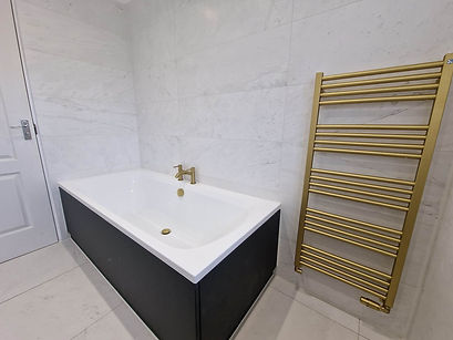 A modern bathroom features a sleek white bathtub with gold fixtures, set against marble tiles