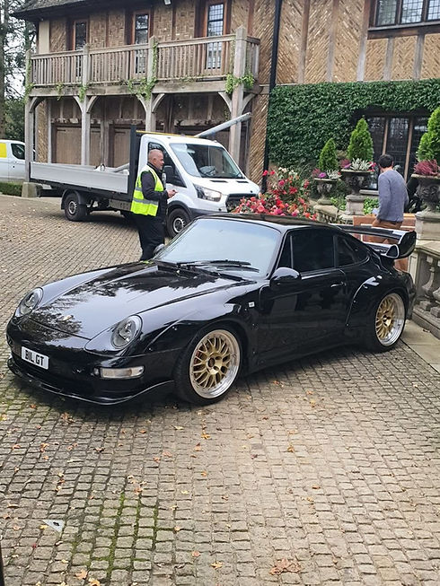 A classic black Porsche sports car parked on a paved driveway outside a residential property