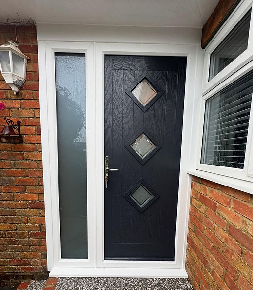 Modern dark grey composite front door with diamond glass panels installed next to a brick wall