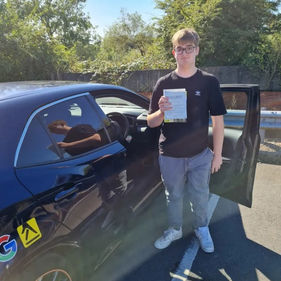 Young man smiles while holding a certificate beside a black car