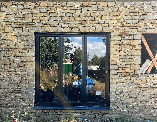 Modern black framed double glazed window fitted into a traditional stone brick wall