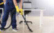 A man in blue overalls and yellow gloves is cleaning a room with a broom and dustpan