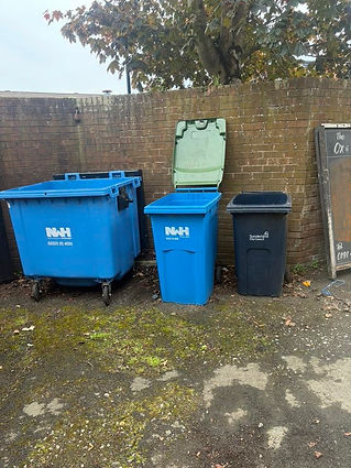 Three blue trash cans positioned beside a textured brick wall