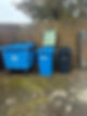 Three blue trash cans positioned beside a textured brick wall