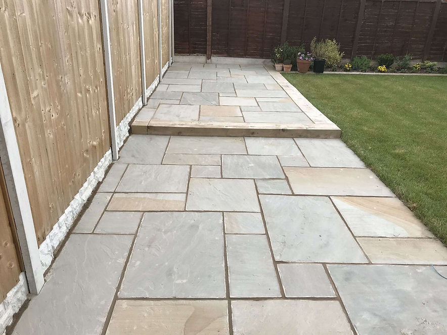 A neatly laid stone pathway runs alongside a fenced yard, leading towards a small step