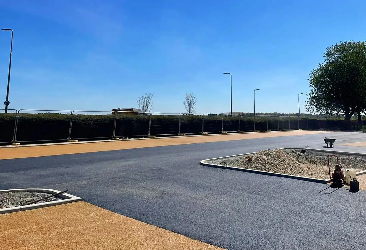 Modern commercial entrance showing smooth black tarmac road surface meeting light gravel paths