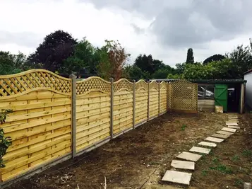 Stepping stone path across a freshly soiled garden next to decorative wave top wooden fence panels