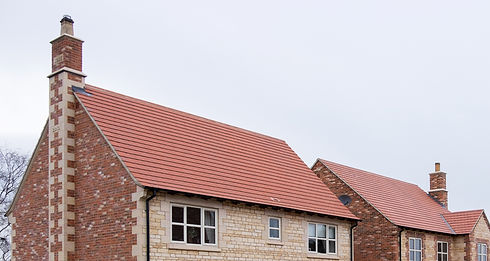 A brick house featuring a red roof and chimney against a clear sky