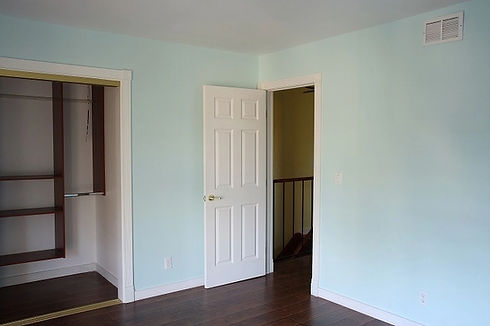 Light blue bedroom with open white wooden door, dark laminate flooring, and built in closet unit