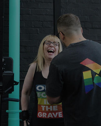 A woman with blonde hair and glasses laughs joyfully, wearing a colorful shirt