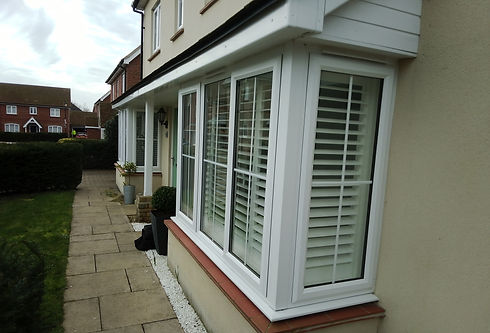 White framed bay window on a cream exterior house wall next to a garden path