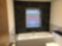 bathroom with black tiled wall, window and a white bathtub and toilet