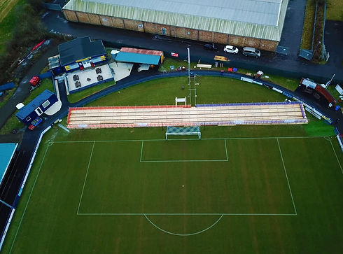 Aerial drone view of a green sports pitch with event scaffolding and temporary structures built alongside it