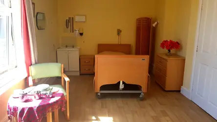 Spacious care home bedroom featuring an adjustable profiling bed and a tea table in the foreground