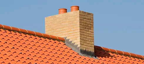 Yellow brick chimney stack with two orange pots on a bright red clay tiled roof