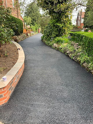 A driveway featuring smooth black asphalt bordered by sturdy brick walls on either side