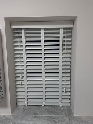 White horizontal window blinds partially open with pull cords on a neutral-toned wall
