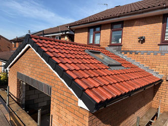 Red-tiled garage roof with a skylight, adjacent to a larger brick house