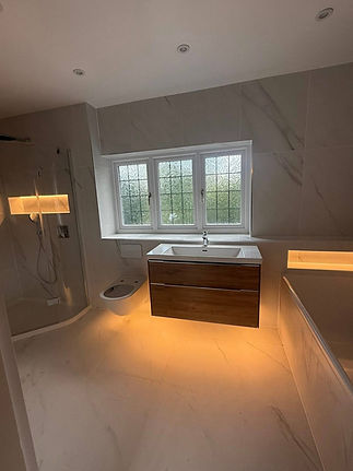 Modern bathroom with a rain shower, backlit glass shelves, and a wall-mounted sink unit under a window