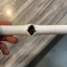 A close-up of a broken white plastic tube, with a jagged, star-shaped hole in the center