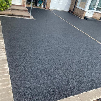 Newly laid black tarmac driveway beside residential property