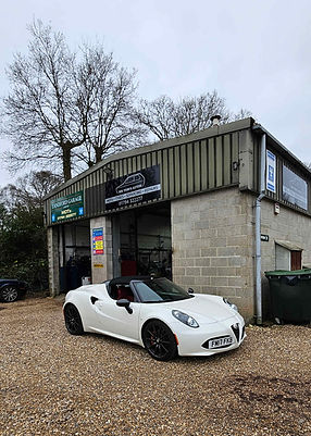 White sports car parked in front of a garage with a brick and metal exterior
