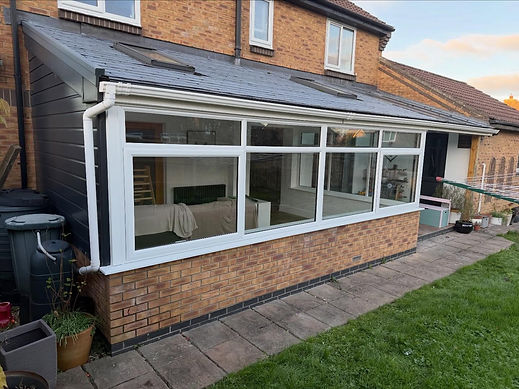 White lean to conservatory extension with a dark tiled roof alongside a garden lawn