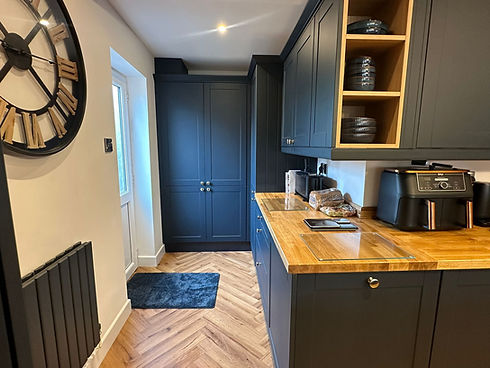 Modern kitchen with matte black cabinets, wooden countertops, and a large wall clock