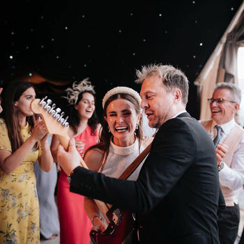 A joyful bride and guests celebrate at a lively party, with the bride smiling widely and a man playing guitar