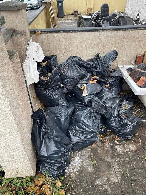 Pile of black plastic rubbish bags stacked outside against a wall