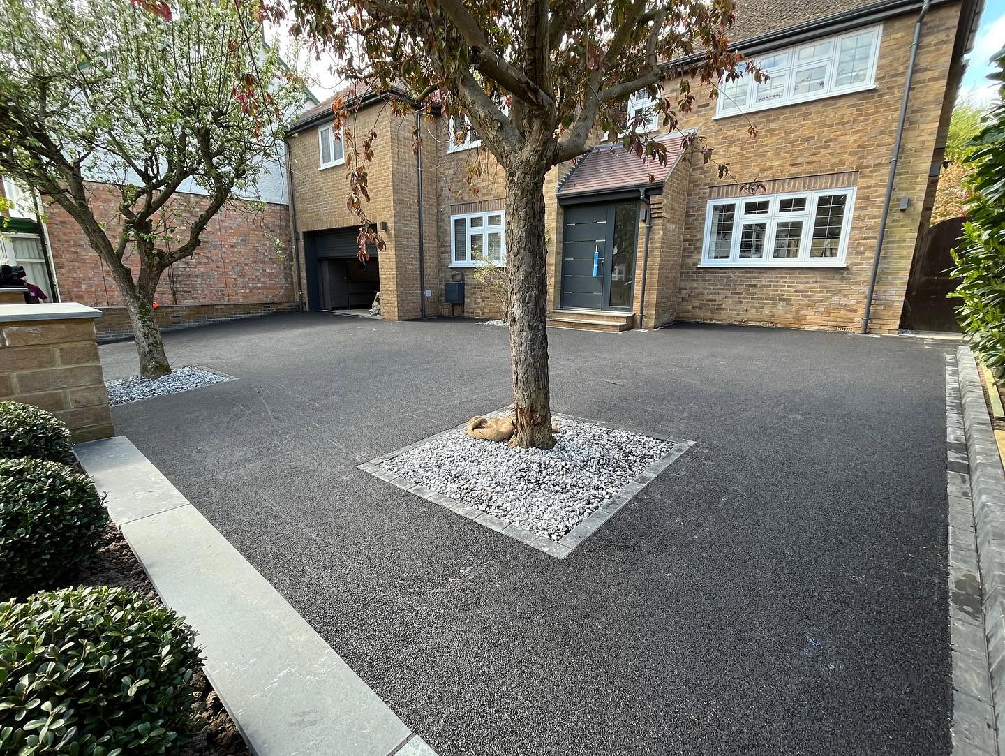 Freshly laid smooth black tarmac driveway featuring decorative stone squares around established trees