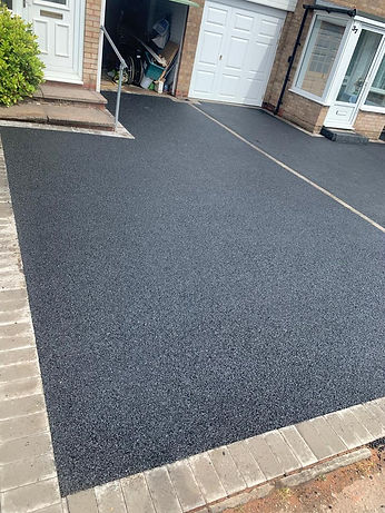 A black asphalt driveway bordered by a sturdy brick wall, showcasing a clean and well-maintained exterior