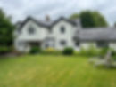 A charming two-story white house with black trim sits amid lush greenery and a manicured lawn