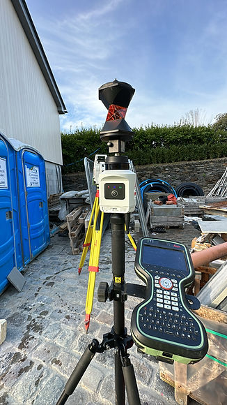 White surveying total station on a black tripod outdoors with blue portable toilets and a bright blue sky