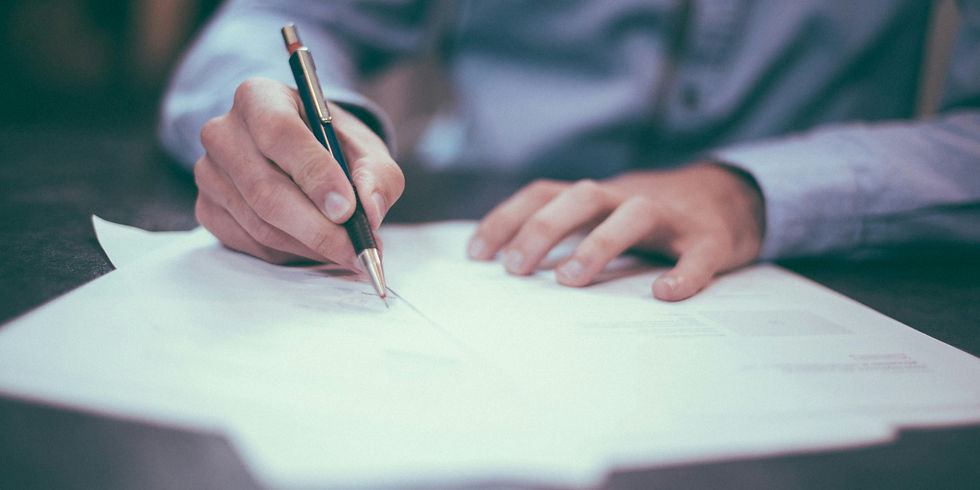 A person diligently signing official documents at a desk, emphasizing the importance of careful review in professional settings.