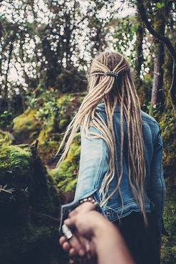 Girl with Dreadlocks walking away, holding a hand and guiding photographer into the wilderness.