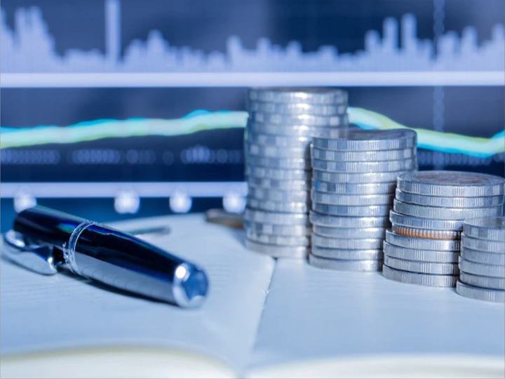 Pilhas de moedas e caneta diante de um gráfico financeiro