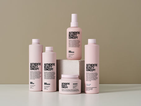 Produkty Authentic Beauty Concept Glow naaranžované v minimalistickém světlém prostředí. Růžová řada určená pro barvené vlasy, která dodává lesk a chrání barvu.