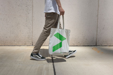 Pessoa caminhando com ecobag branca estampada com a marca Syntetiza em verde