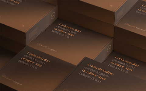 Caixas de embalagem Roberta Pozzobom em marrom escuro com texto "Cada detalhe define sua beleza única"