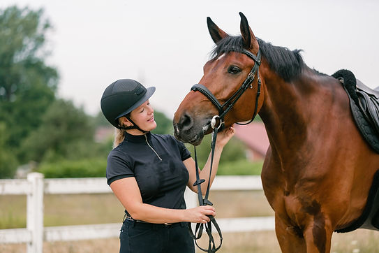 Young female jockey in helmet petting her horse in countryside.jpg