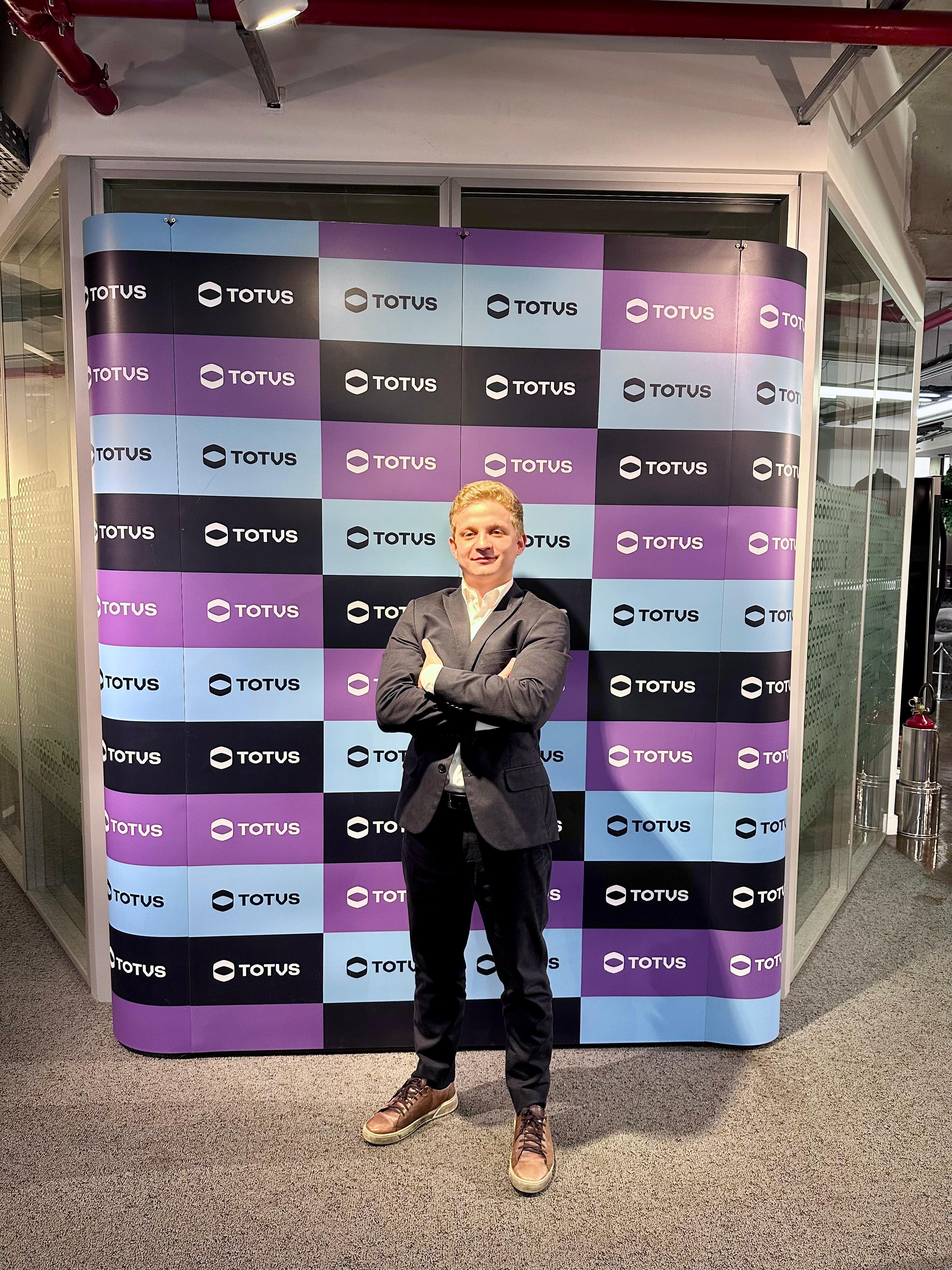 foto de um homem loiro vestindo um terno azul marinho de braços cruzados