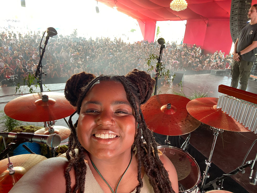Versatile drummer Aisha Gaillard performing on stage, brightly lit, with a band or large audience in the background.