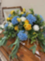 silk casket spray with blue hydrangeas, yellow roses and white peonies on a wooden casket