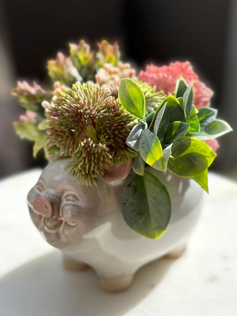 Neutral-toned silk floral home decor arrangement in a happy smiling pig vase. Razorback themed.